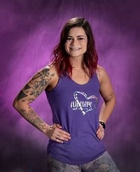 Smiling woman in purple tank top posing with hands on hips against a purple background