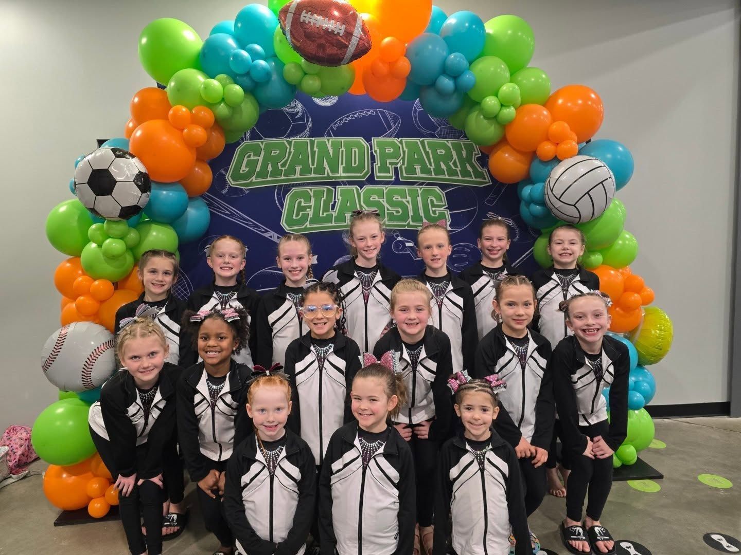 Cheer team posing in front of colorful balloon arch with a “Grand Park Classic” sign