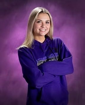Person in a purple hoodie smiling with arms crossed against a purple studio backdrop