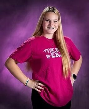 Young person posing with hand on hip, wearing a pink T-shirt against a purple studio backdrop.