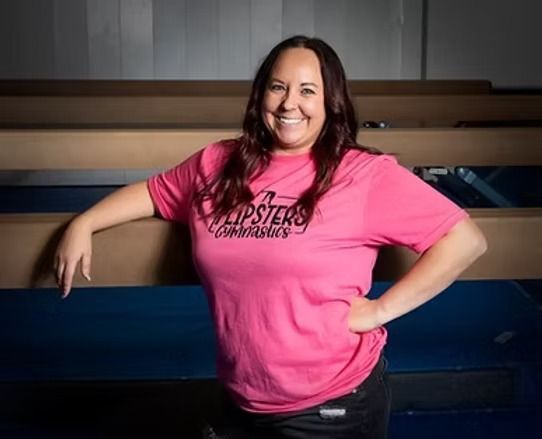 Woman in a pink T-shirt smiling and leaning on a blue bench indoors.