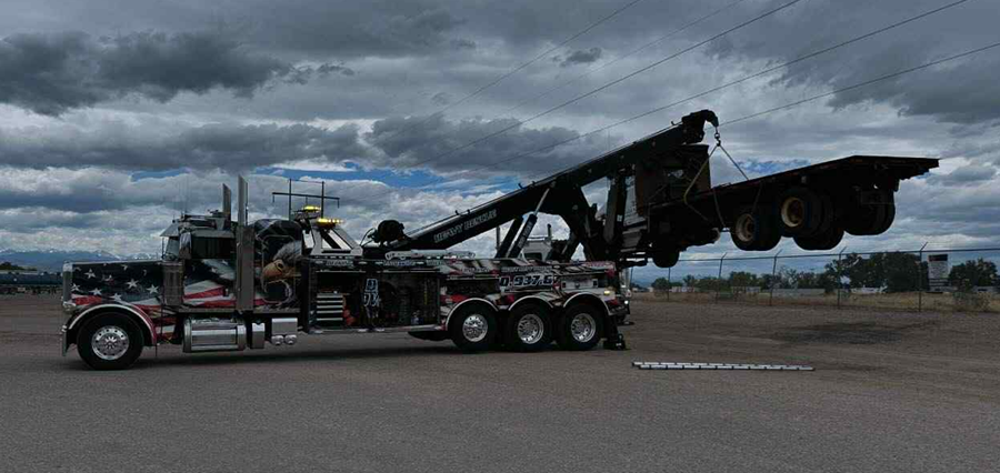 Tow truck lifting a flatbed trailer against a cloudy sky.