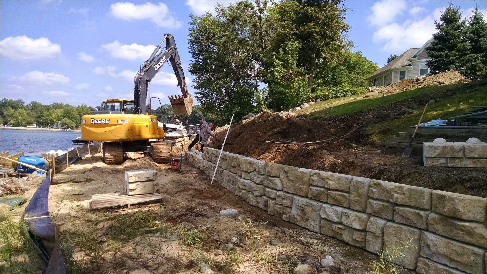 Yellow excavator working on a riverside retaining wall under a blue sky