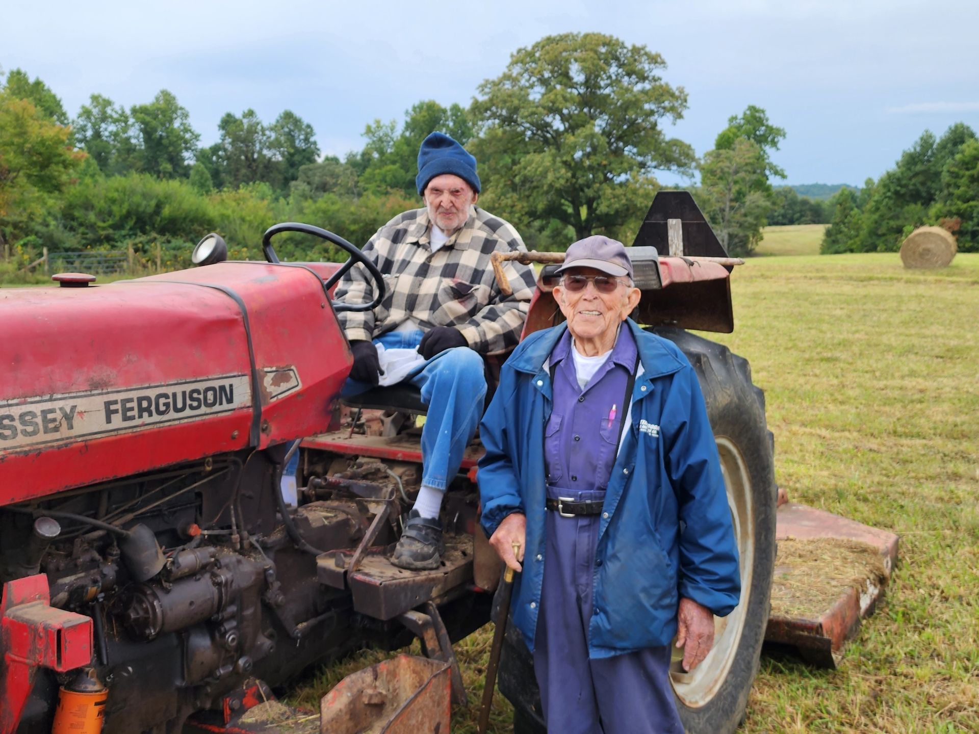 Two men on a red Massey Ferguson tractor in a field. One man is driving. Blue sky.