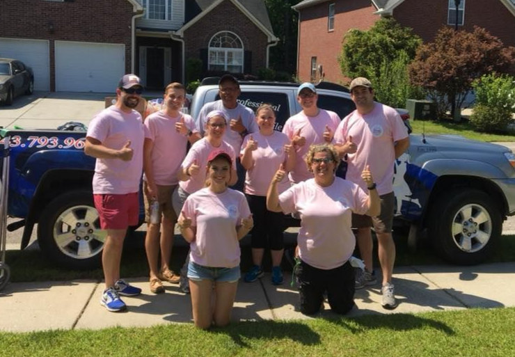 Group of people in pink shirts posing in front of a blue pickup truck on a driveway