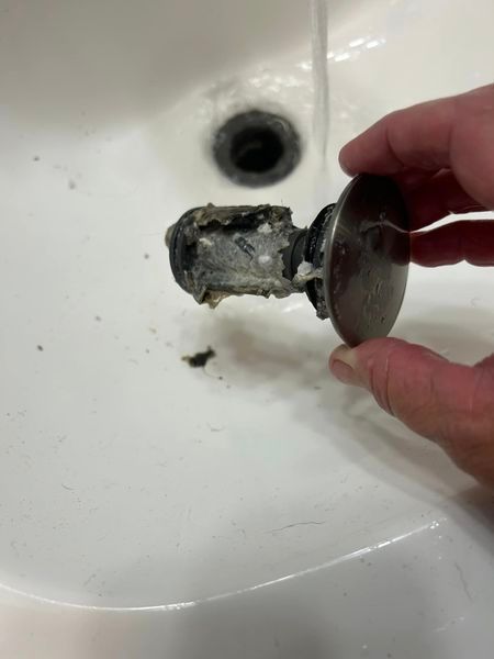 A person is holding a drain plug in their hand over a sink.
