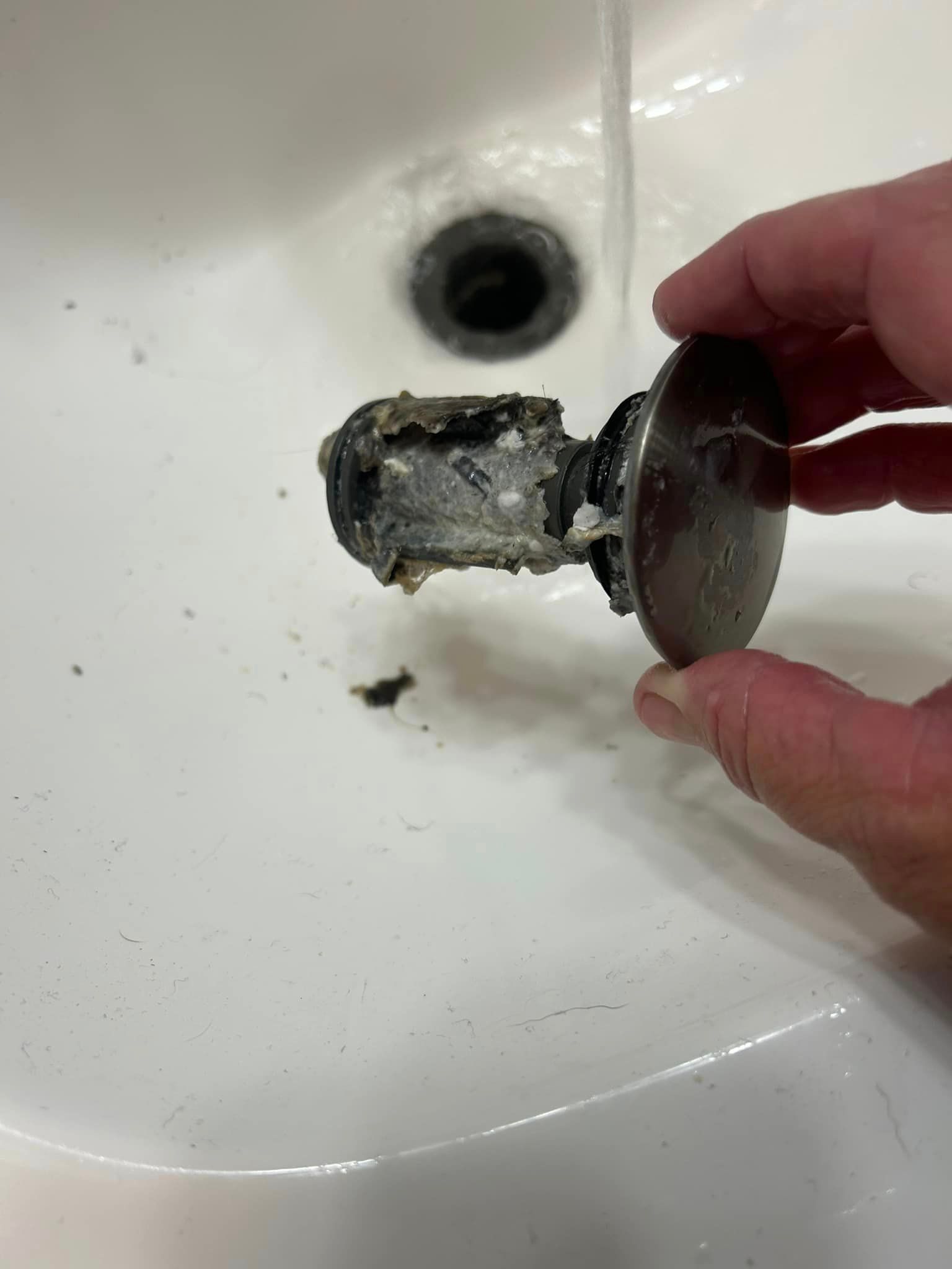 A person is holding a drain plug in front of a sink.