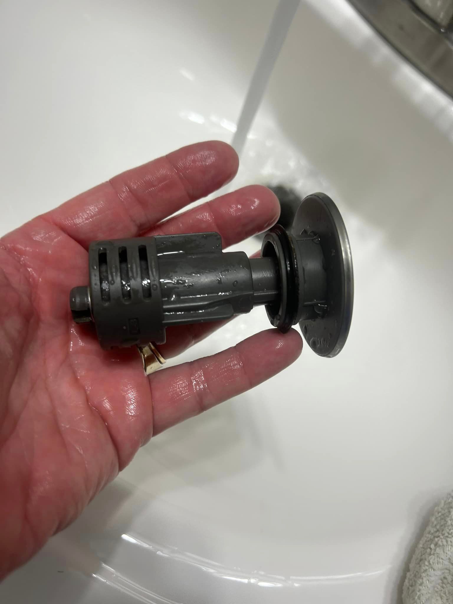 A person is holding a small object in their hand in front of a sink.