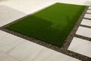 Rectangular green lawn bordered by stone pavers and gravel in a modern courtyard