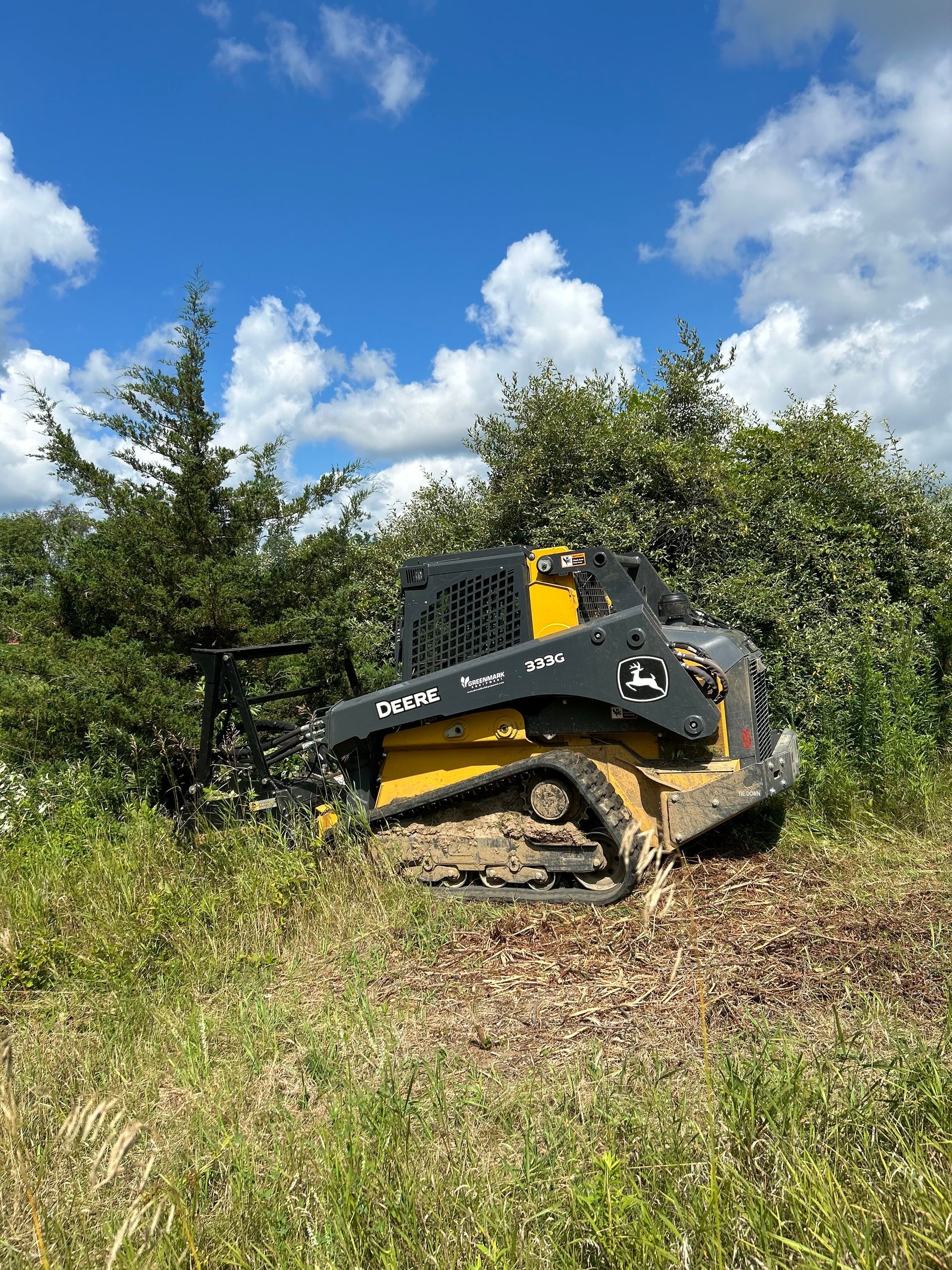 Black-and-yellow skid steer pushing dirt on a grassy hillside under a blue sky