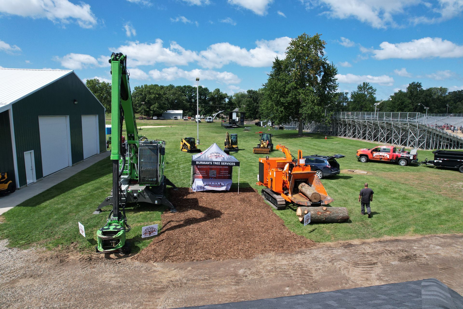 Miniature construction vehicles and excavators displayed on a grassy field near a barn under a blue sky