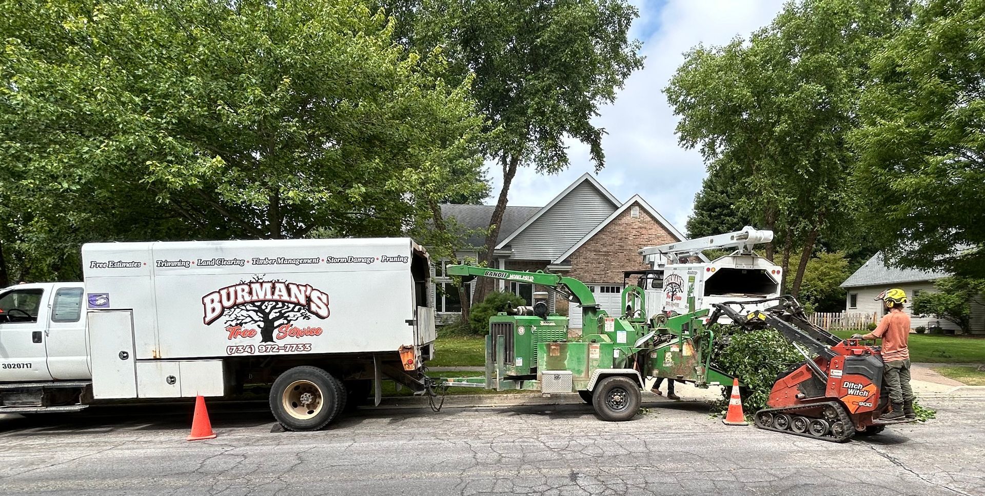 Work truck and small tractor in a yard beside a house, with workers and equipment nearby
