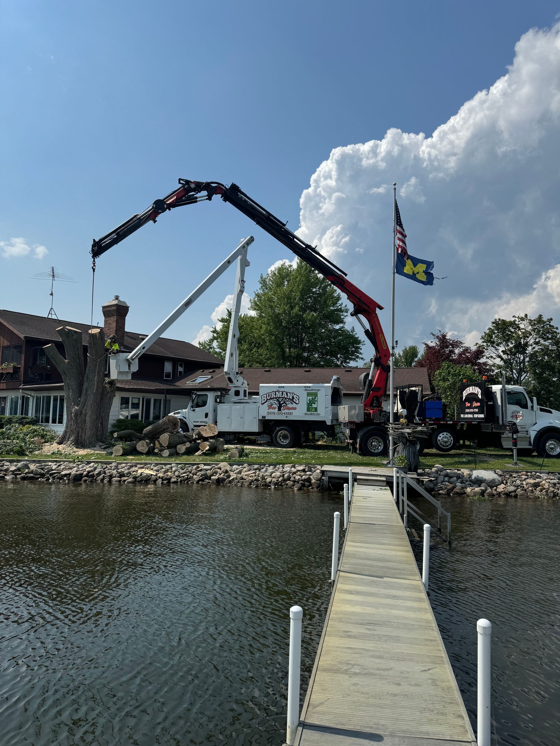 Crane truck on a waterfront dock beside a flagpole and buildings under a partly cloudy sky
