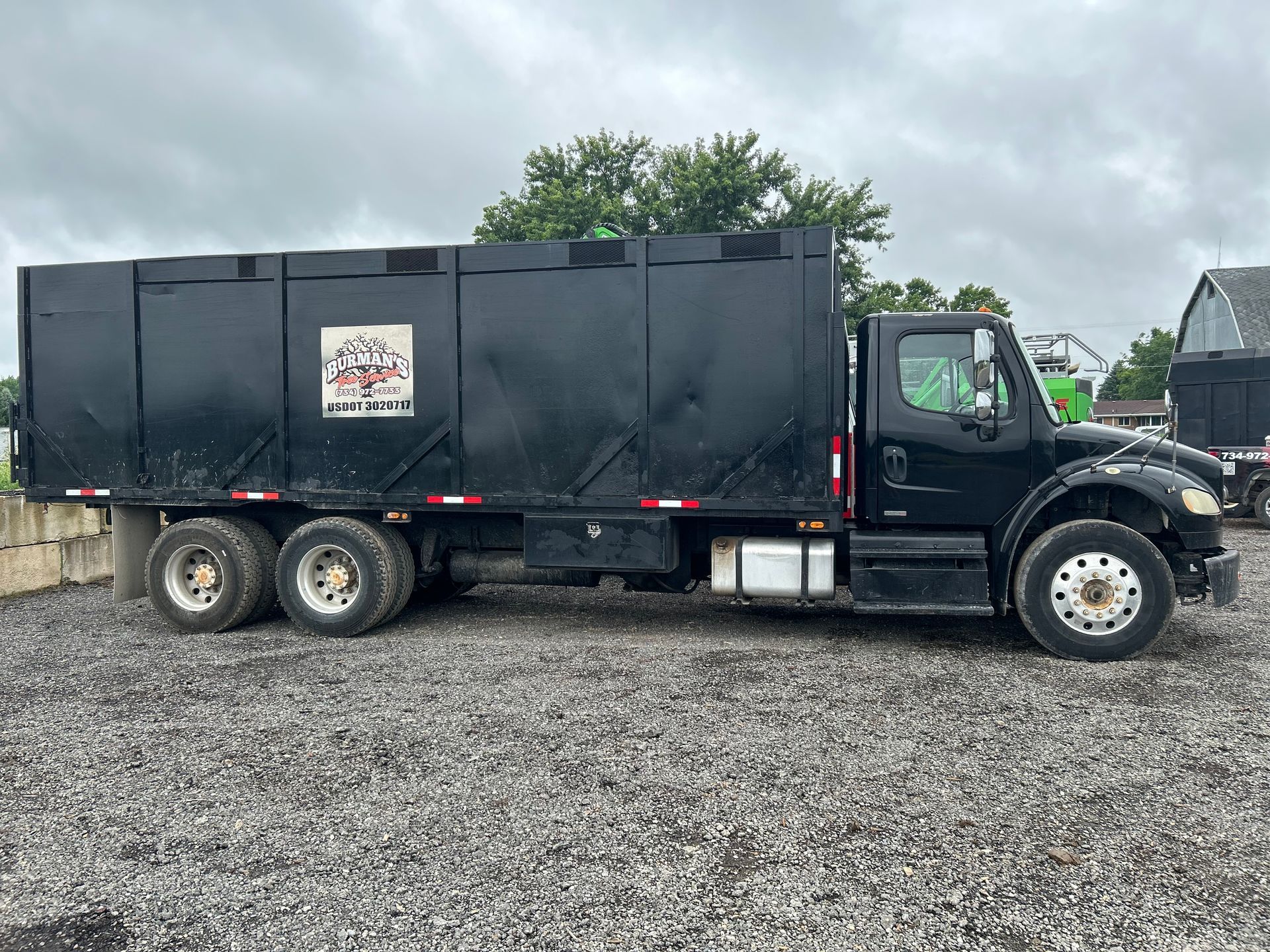 Black dump truck parked on gravel under a cloudy sky