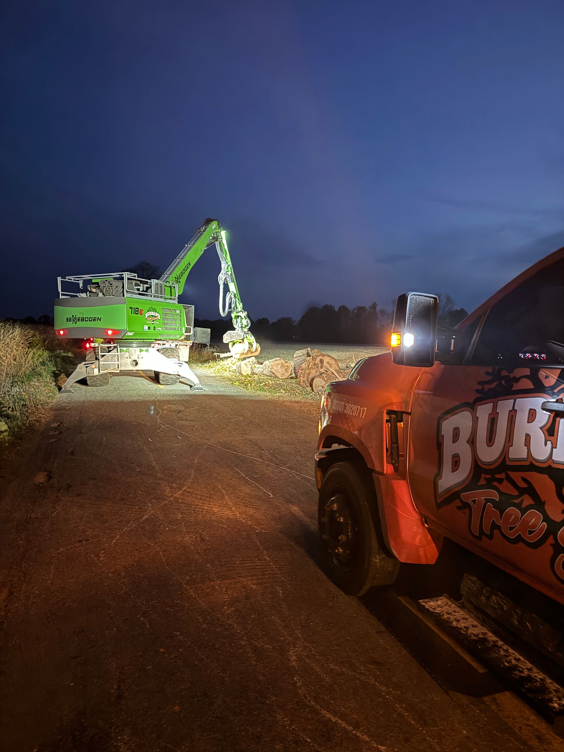 Nighttime scene with a green excavator clearing rubble and a damaged orange truck in the foreground