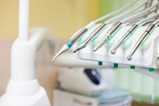 Strumenti odontoiatrici su un vassoio accanto a una poltrona odontoiatrica bianca sfocata e alle relative apparecchiature