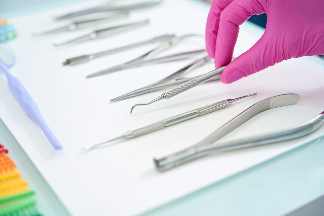 Mano guantata che sceglie uno strumento odontoiatrico in metallo da una fila di strumenti sterilizzati su una superficie bianca