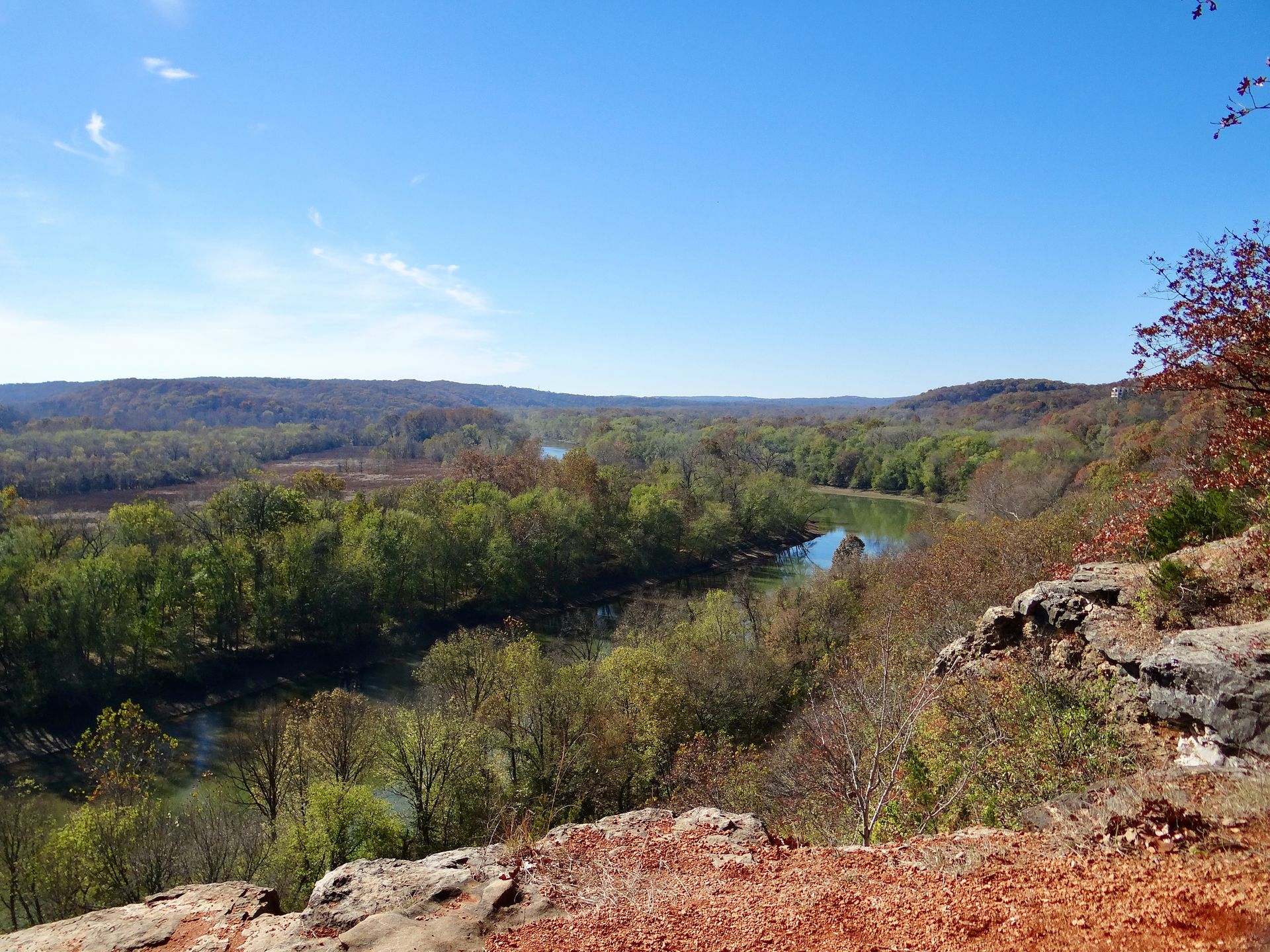 A view of a river surrounded by trees from a rocky cliff.