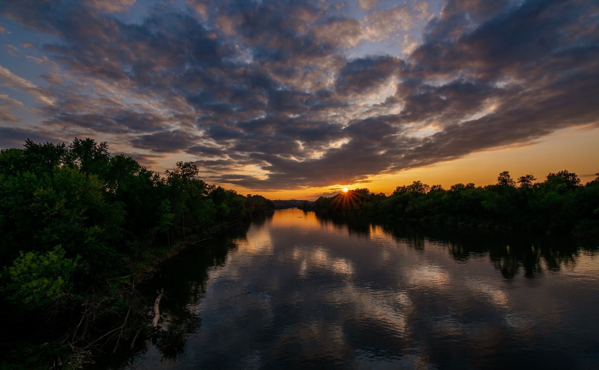 The sun is setting over a river surrounded by trees.