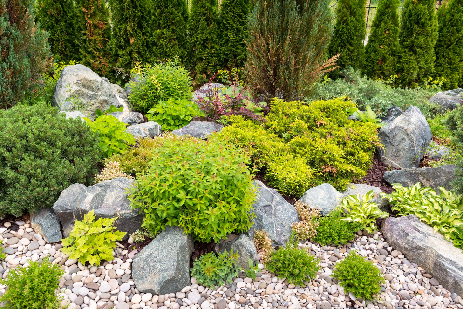 Rock garden with green shrubs, gray stones, and gravel in a landscaped yard
