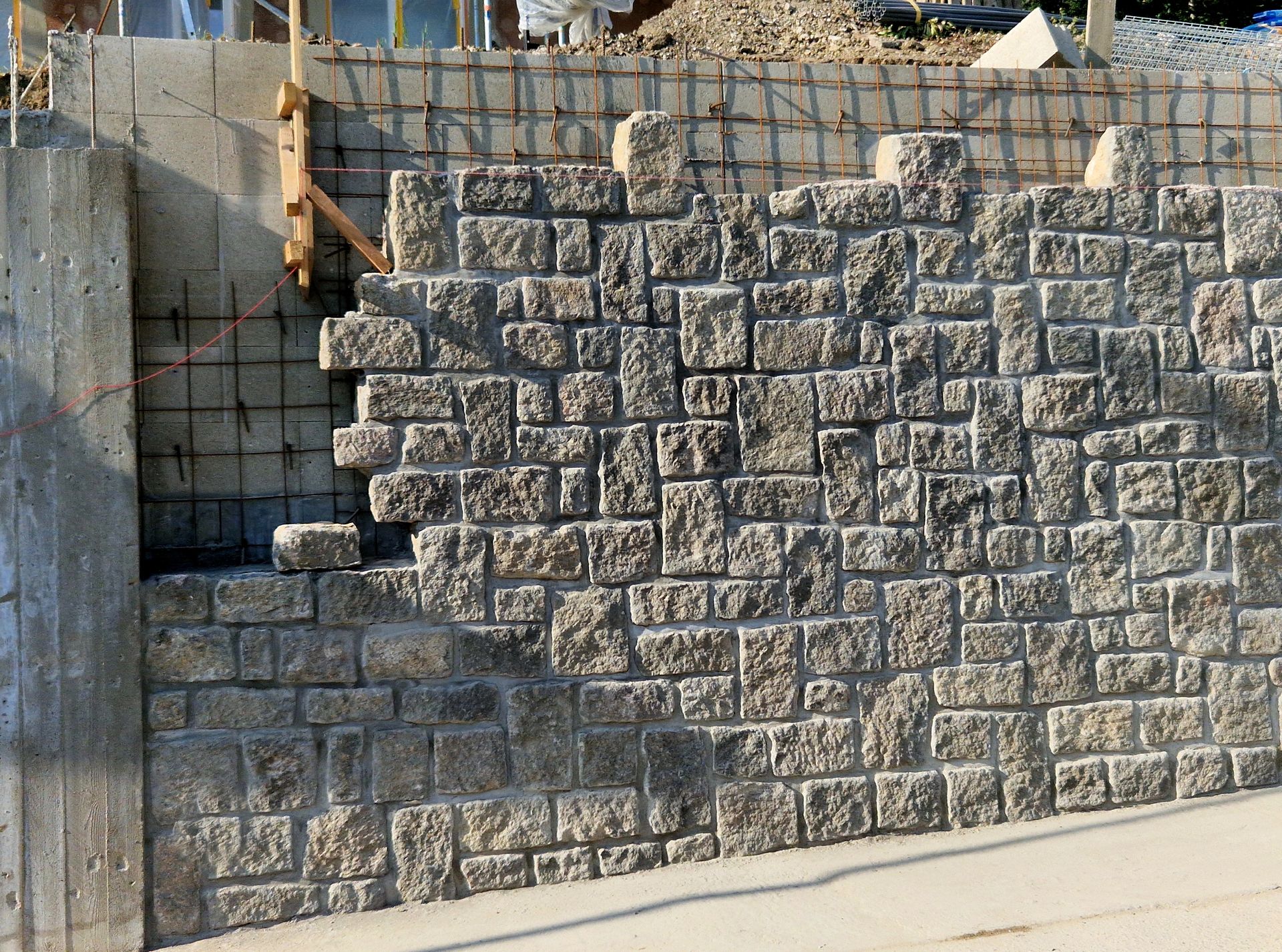 Stone retaining wall with a stepped notch beside a sidewalk and fence