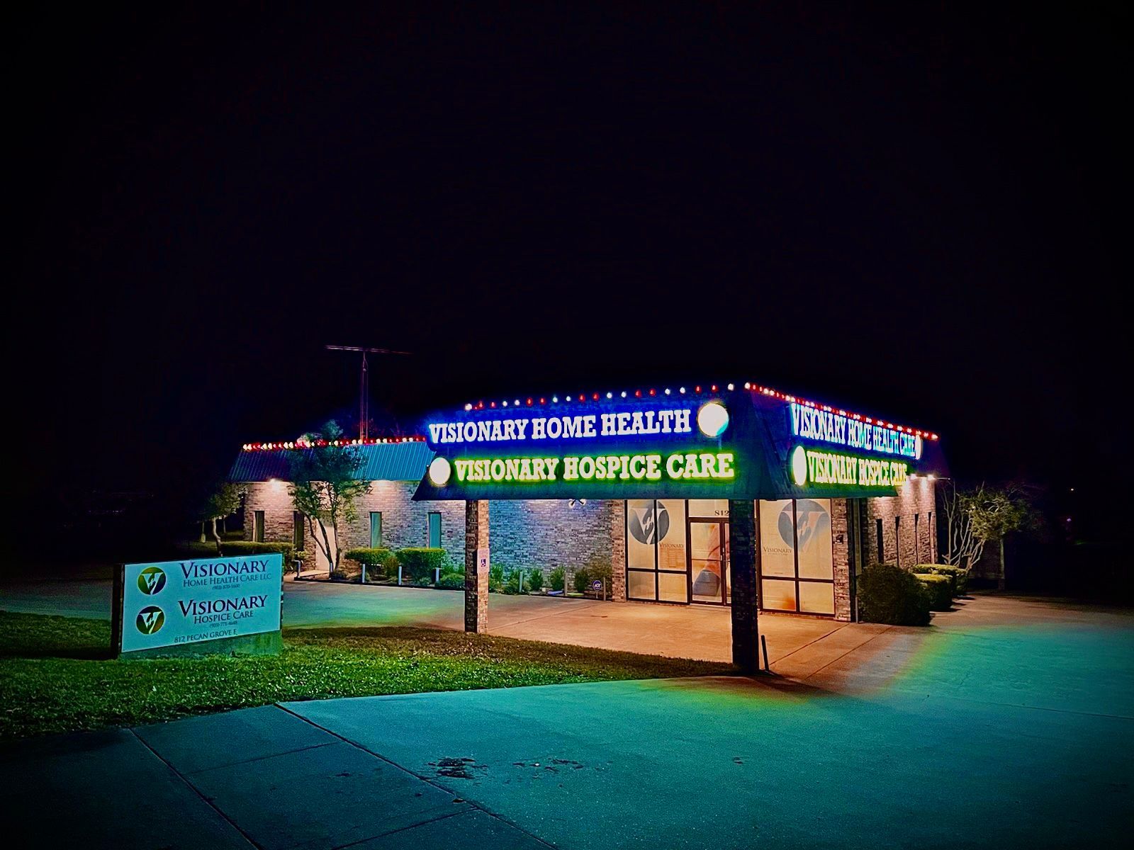 Night-lit entrance sign for a hospice care facility with blue-green lighting and landscaped grounds
