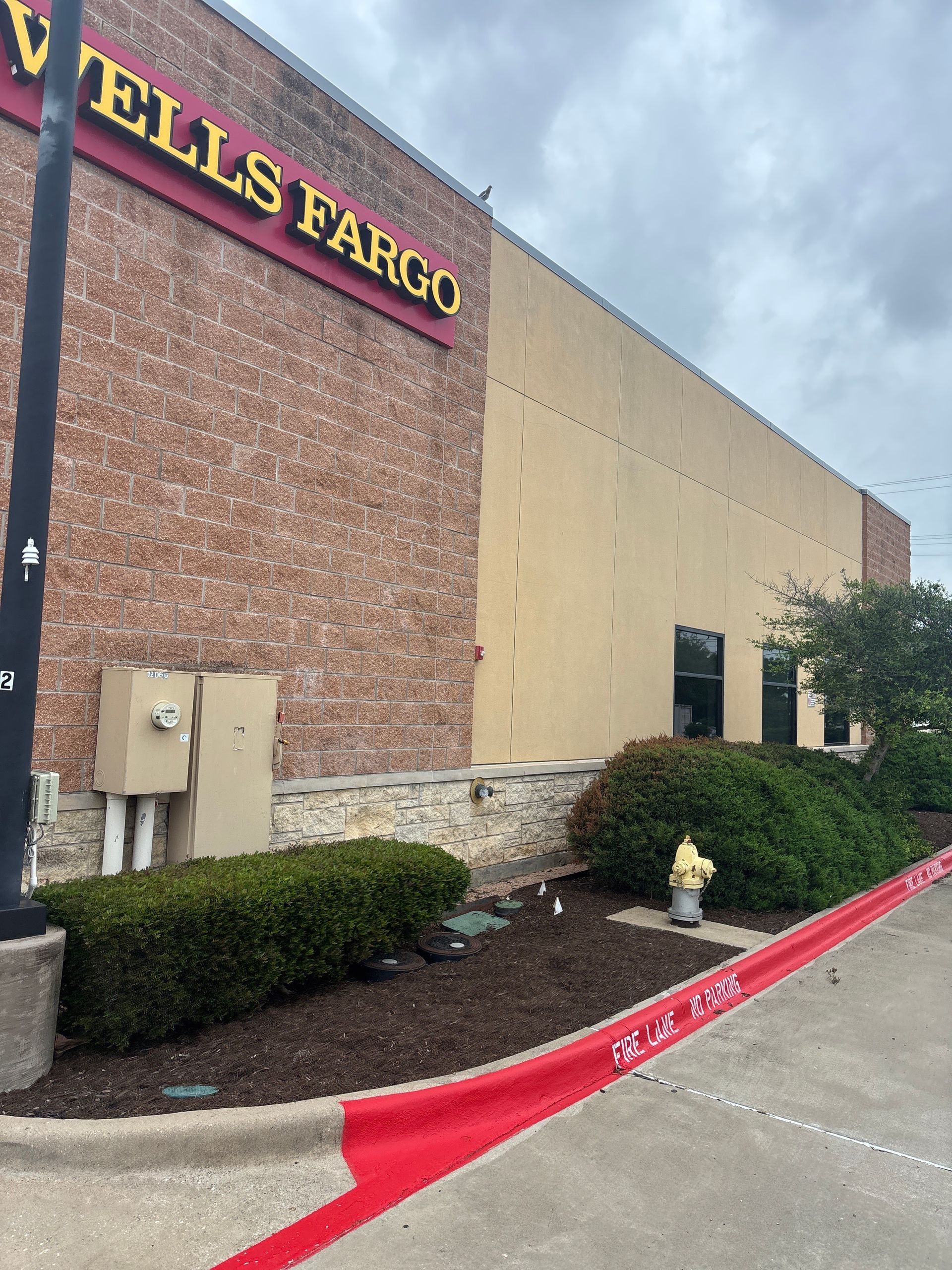 Wells Fargo storefront with brick and beige exterior, red curb, bushes, and a parking lot