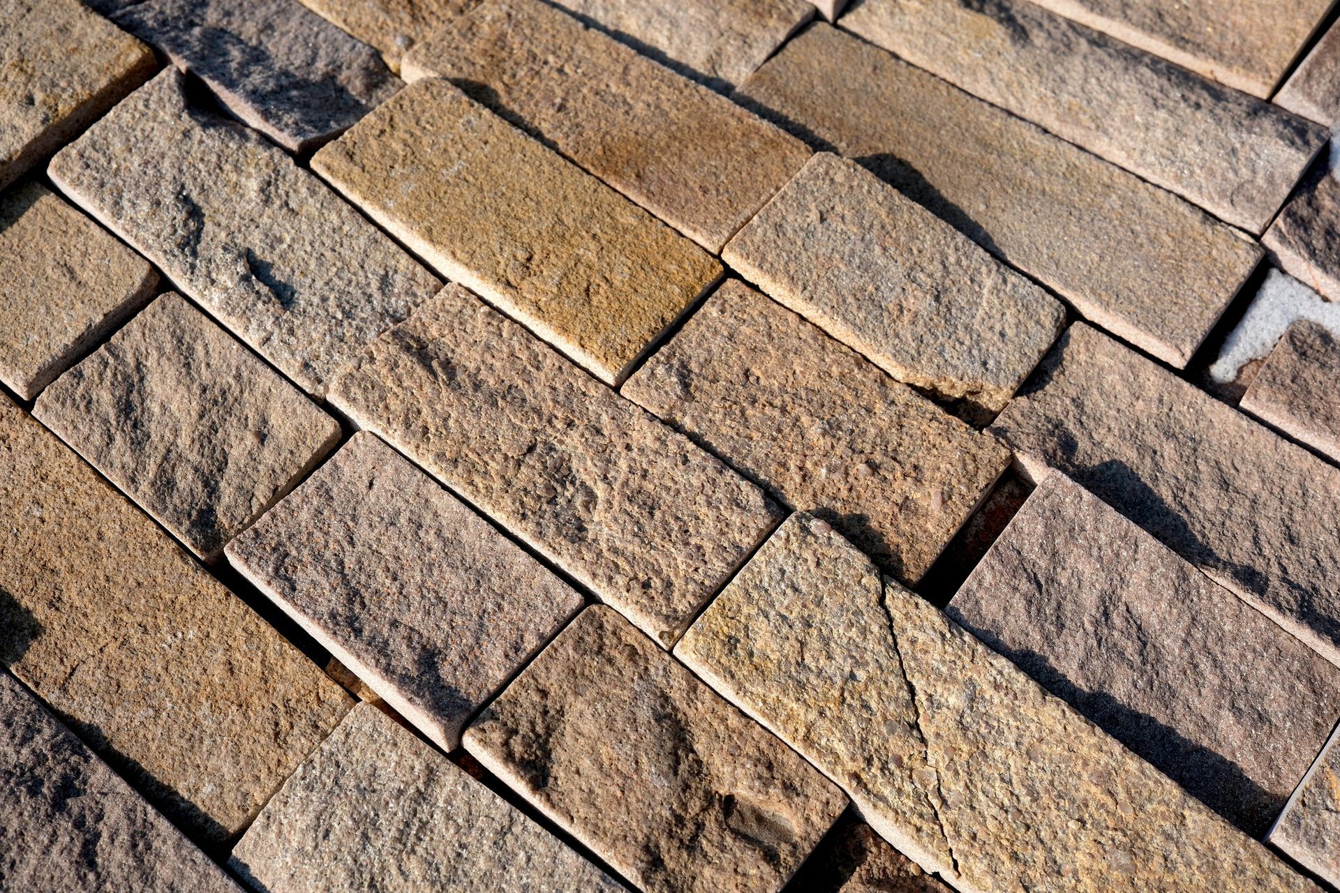 Close-up of tan brick pavers laid in a staggered pattern, with some cracked and weathered stones