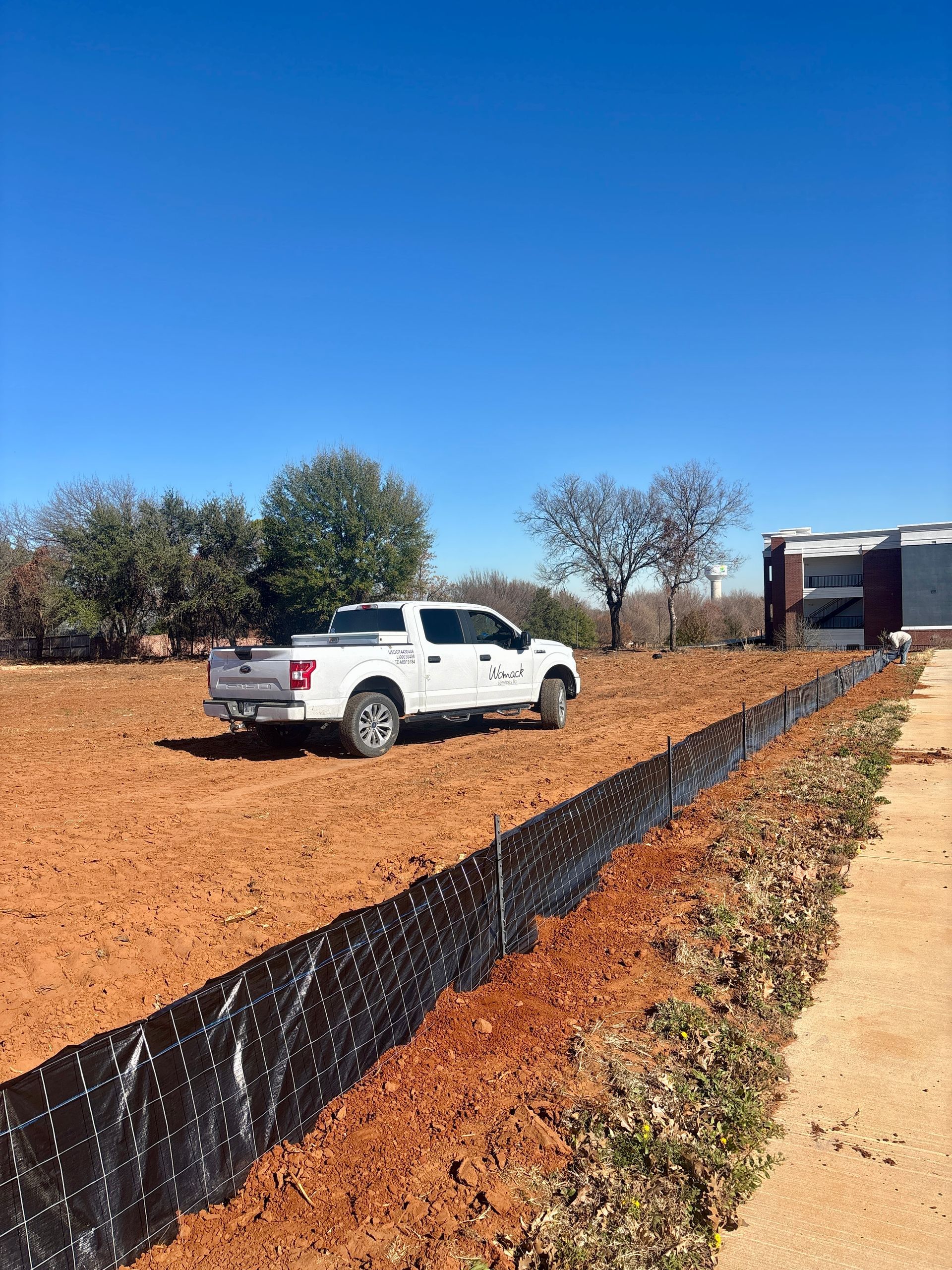 White pickup truck on a dirt road beside a black silt fence under a clear blue sky