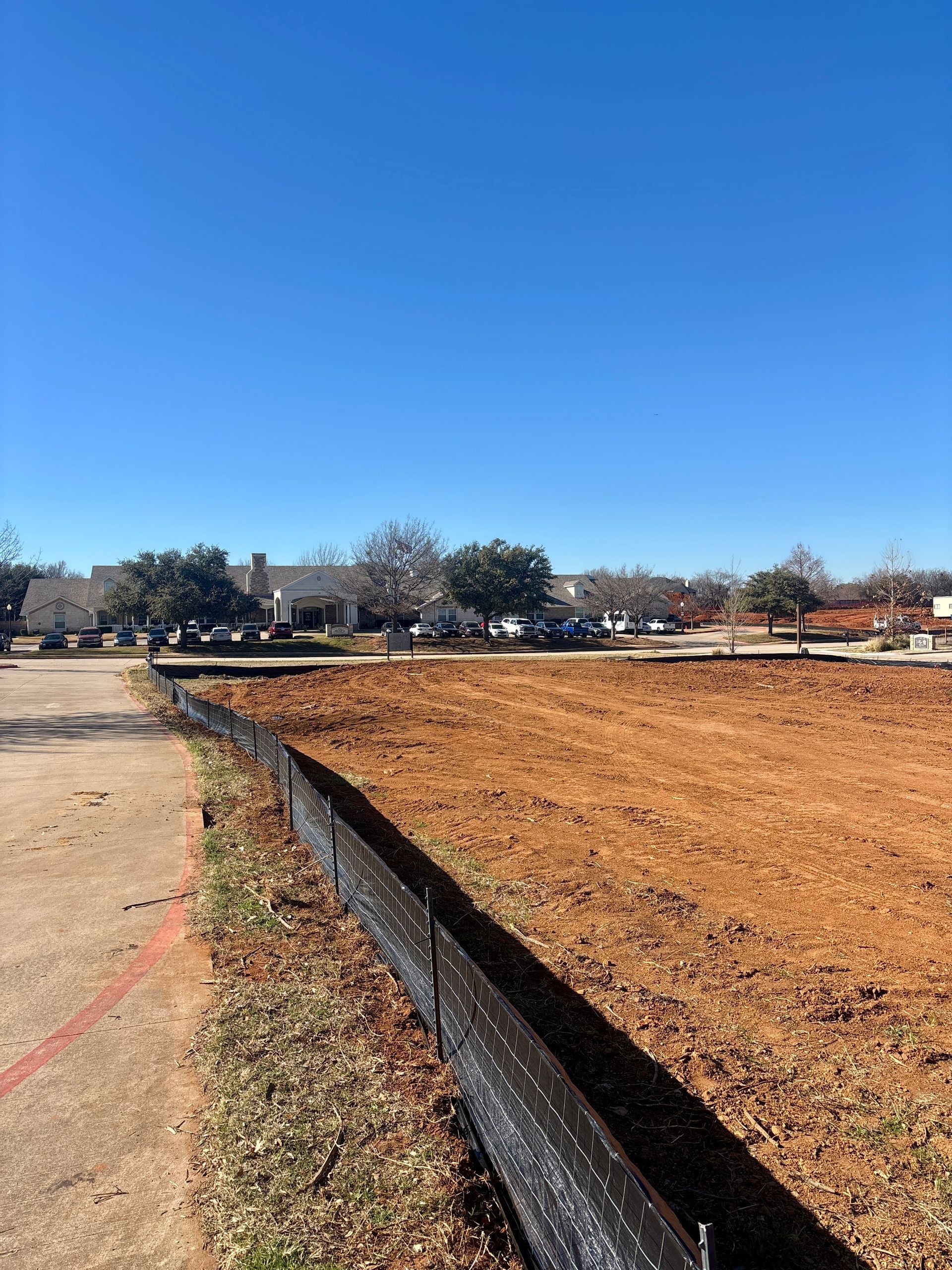 Dry field bordered by a black tarp under a clear blue sky, with trees and houses in the distance.