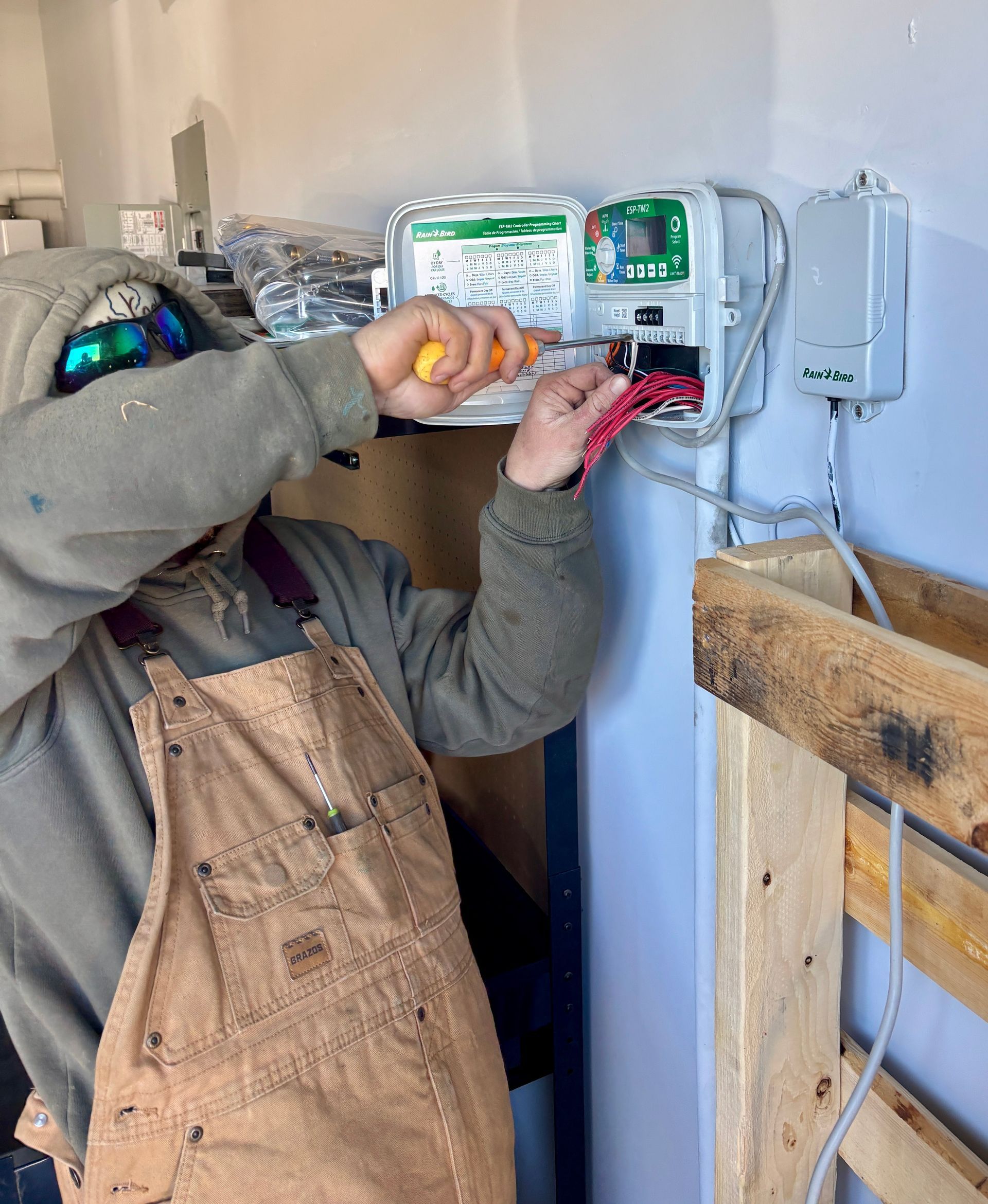 Electrician wiring a wall-mounted control panel with tools in a workshop.