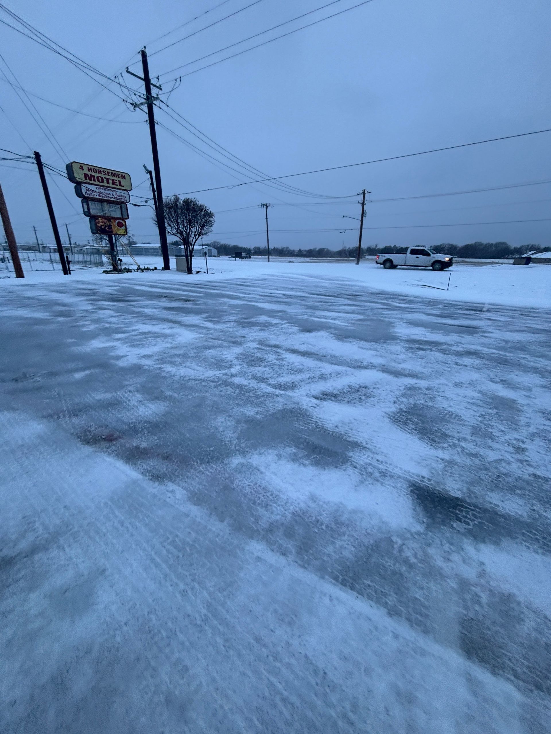 Snow-covered icy road beside power lines and a roadside sign under a gray winter sky