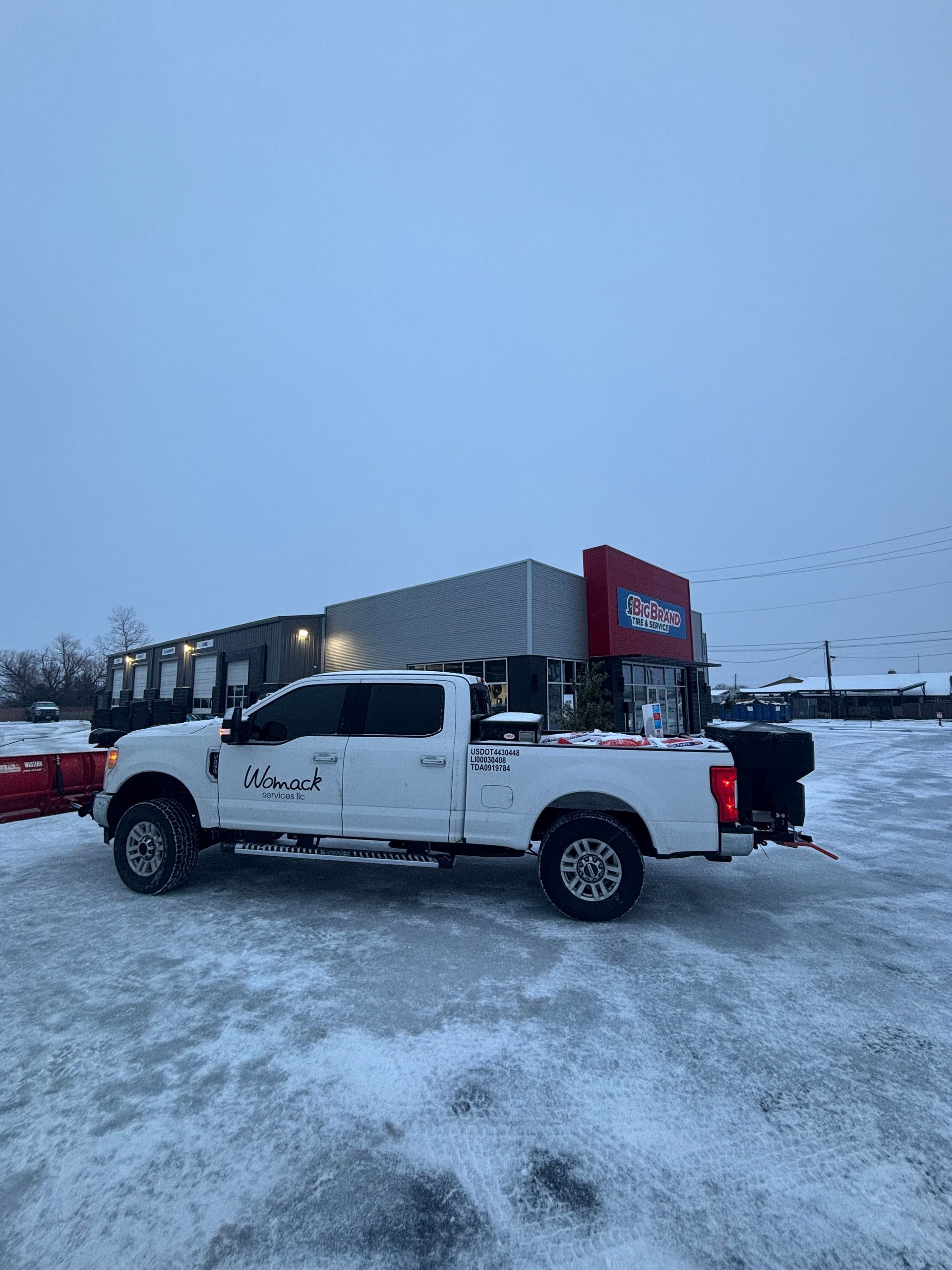 White pickup truck parked in a snowy lot near a building under an overcast sky