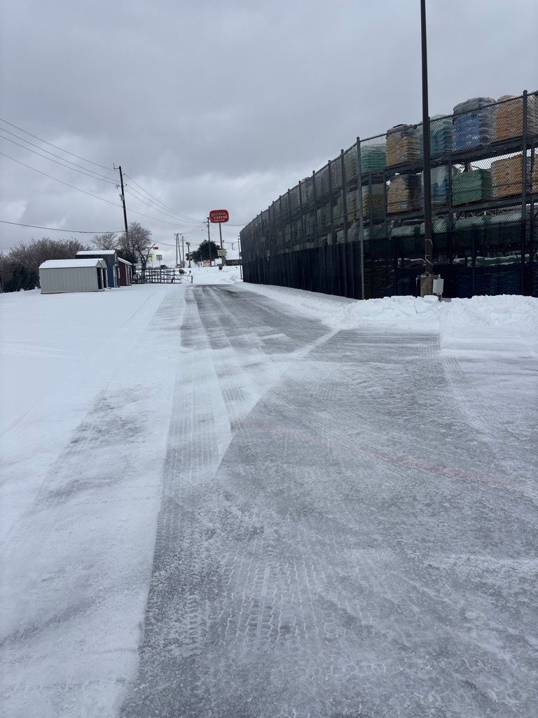 Snow-covered path beside a fenced industrial lot under a gray sky