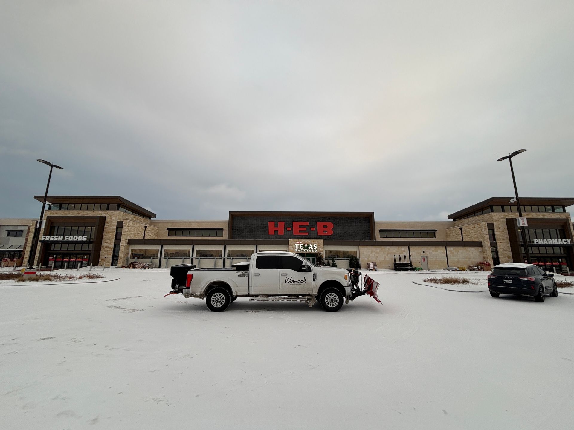 Snowy H-E-B storefront with a white pickup truck parked in front under an overcast sky