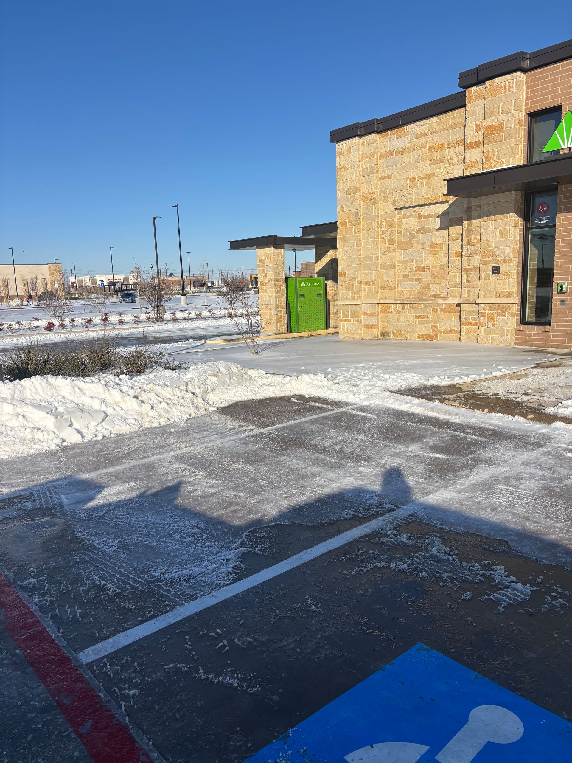 Snowy parking lot beside a stone building under a clear blue sky