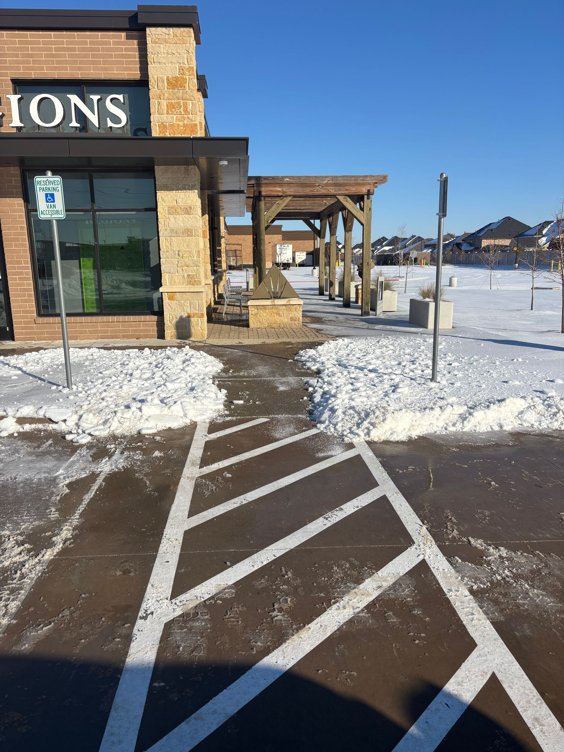Snowy storefront entrance with striped accessibility ramp and parking lot under clear blue sky