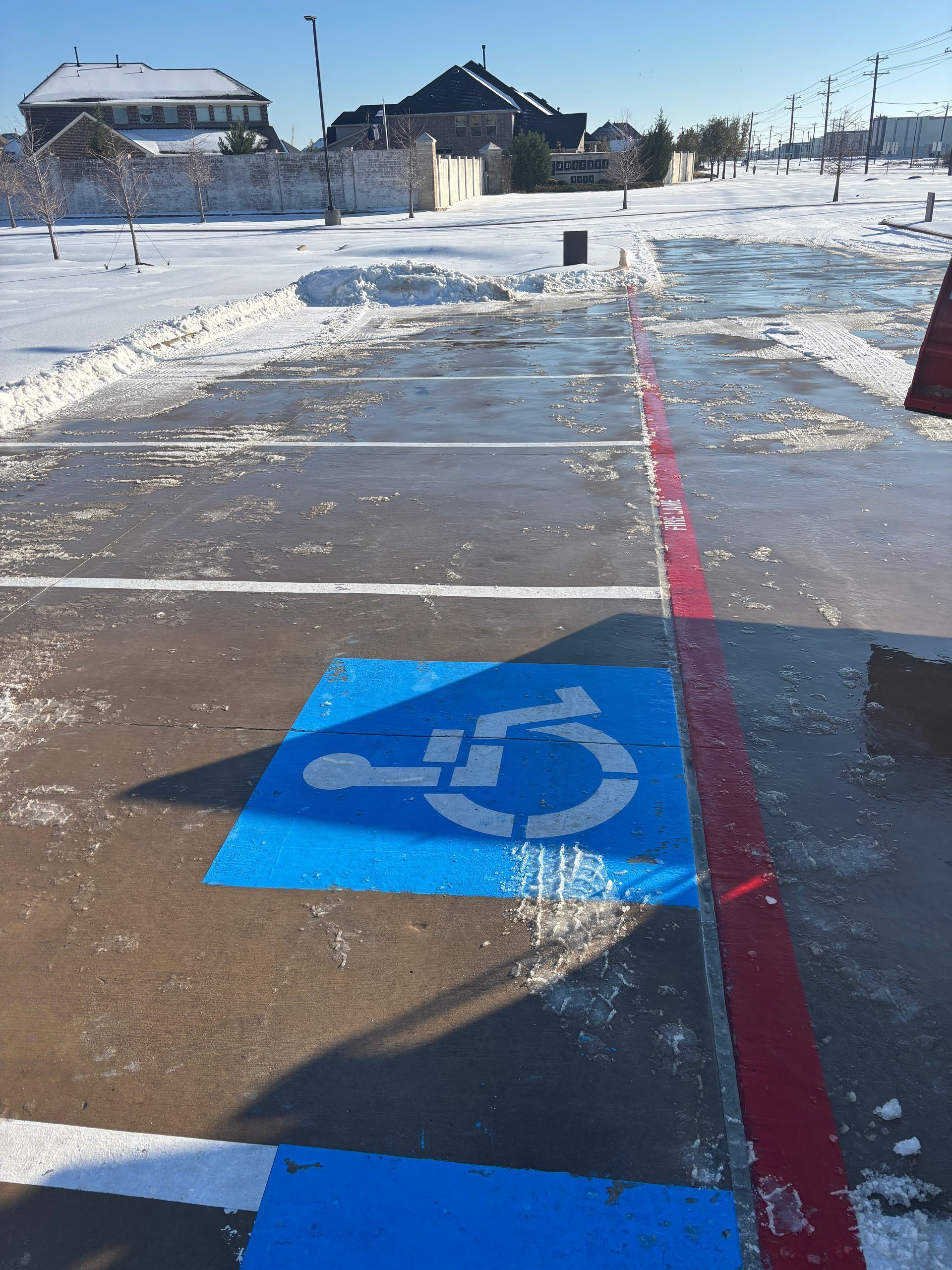 Snowy accessible parking space with blue wheelchair symbol and red boundary line on wet pavement