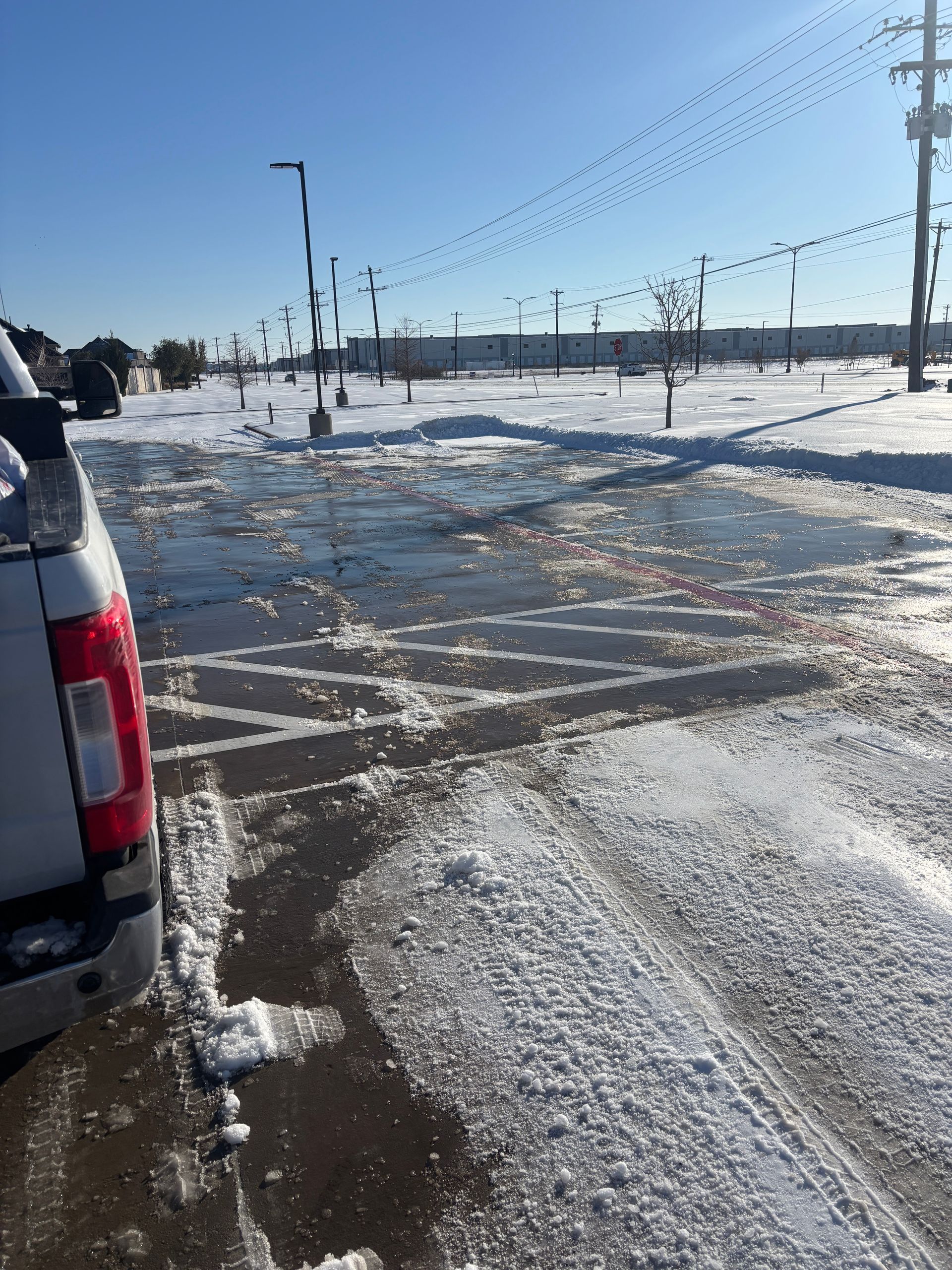Snowy parking lot with icy pavement, a parked SUV, and utility poles under a clear sky