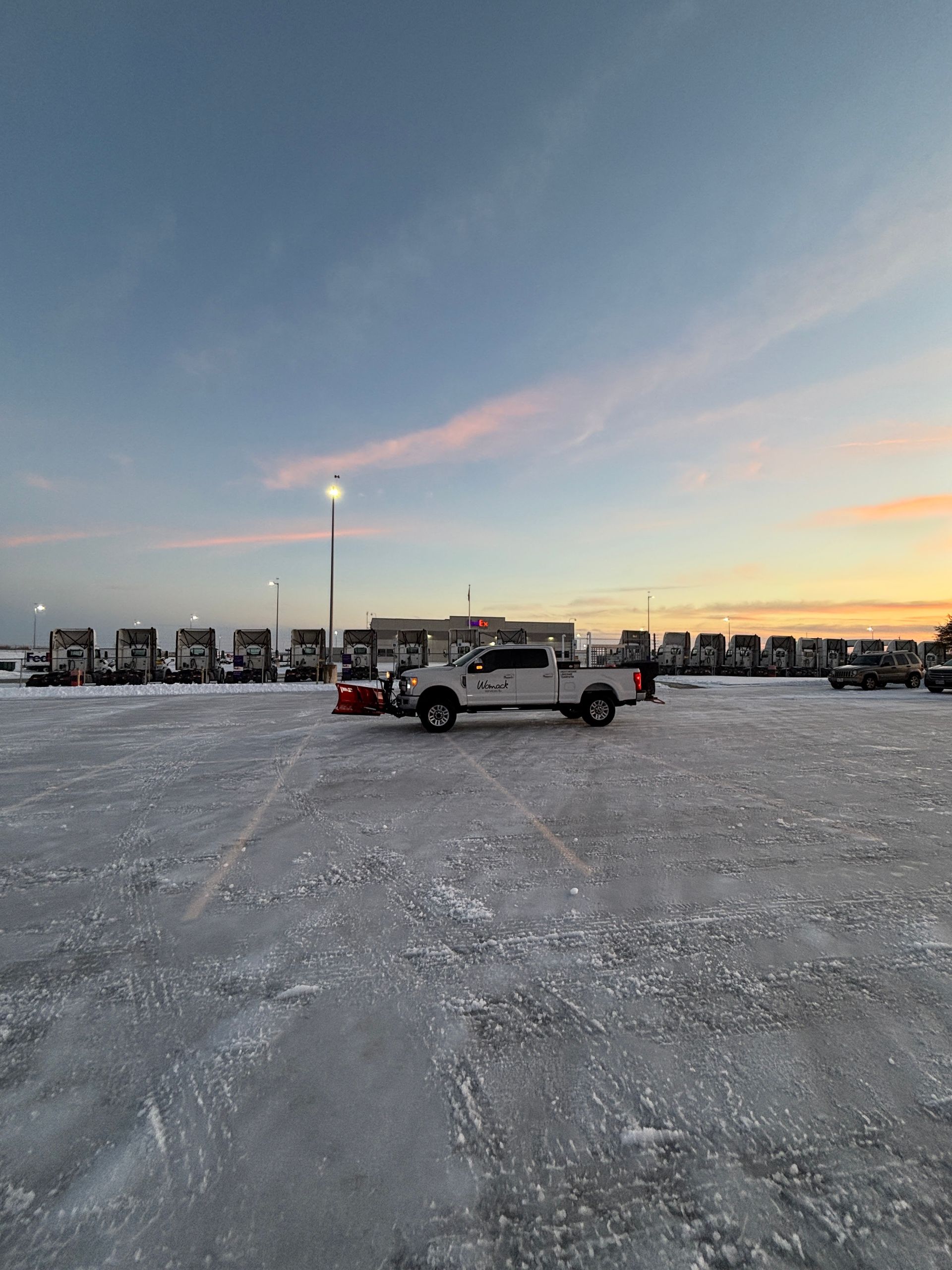 Pickup truck parked on a snowy lot at sunset with a row of RVs in the background