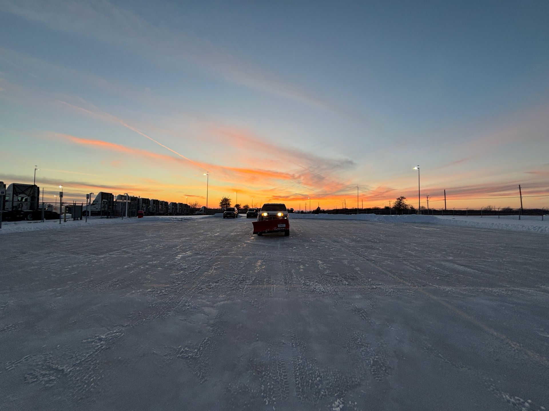 Car driving across a snowy flat at sunset with orange and blue sky