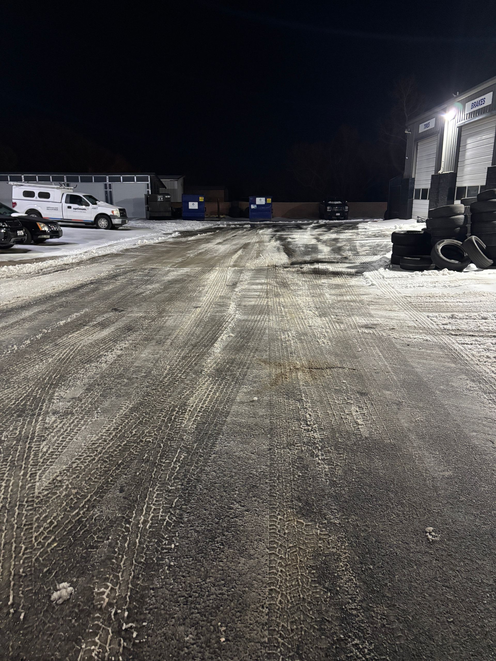 Snowy industrial lot at night with parked vehicles and a building on the right