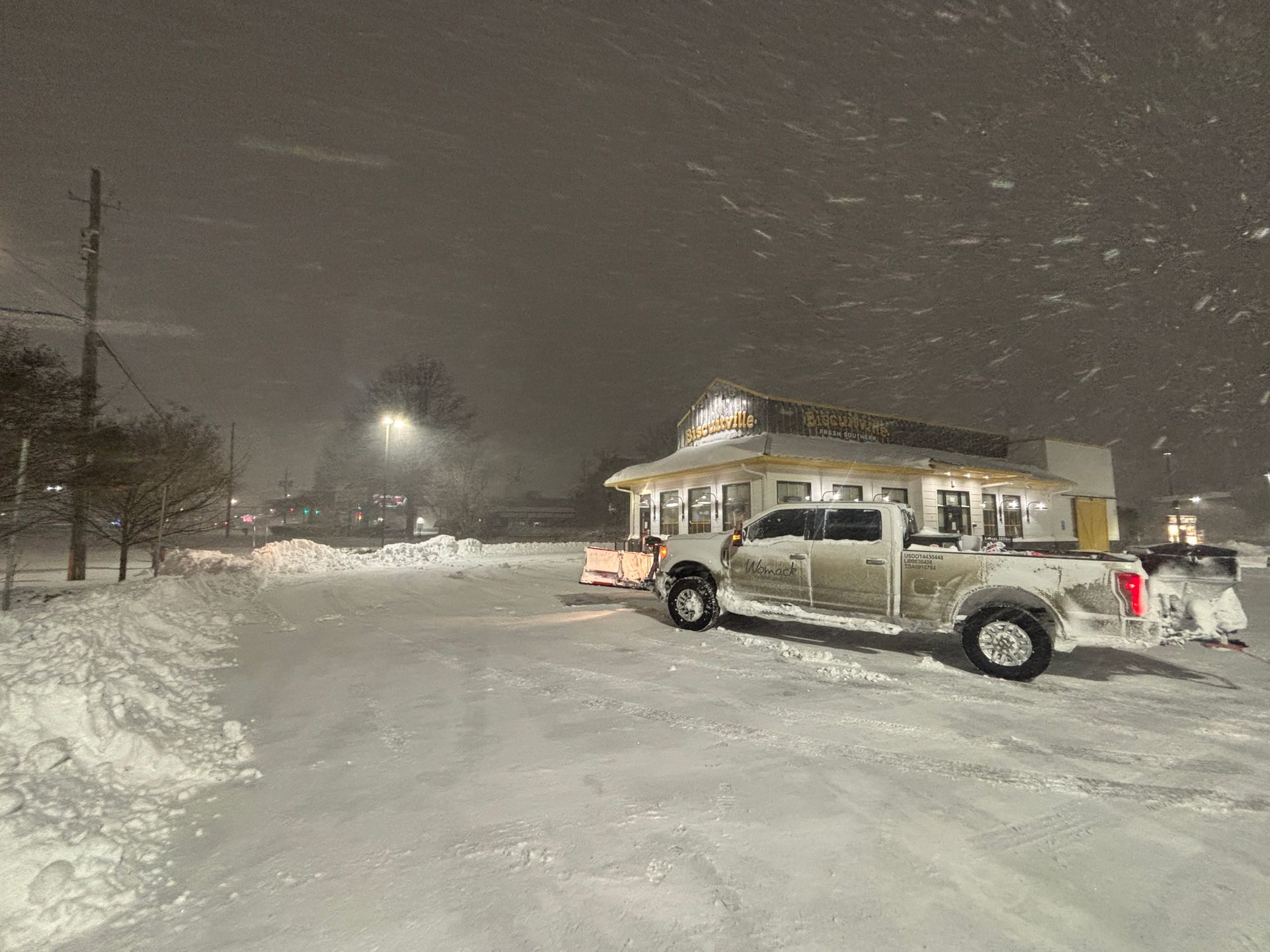Snowy parking lot at night with a pickup truck and lit building during snowfall