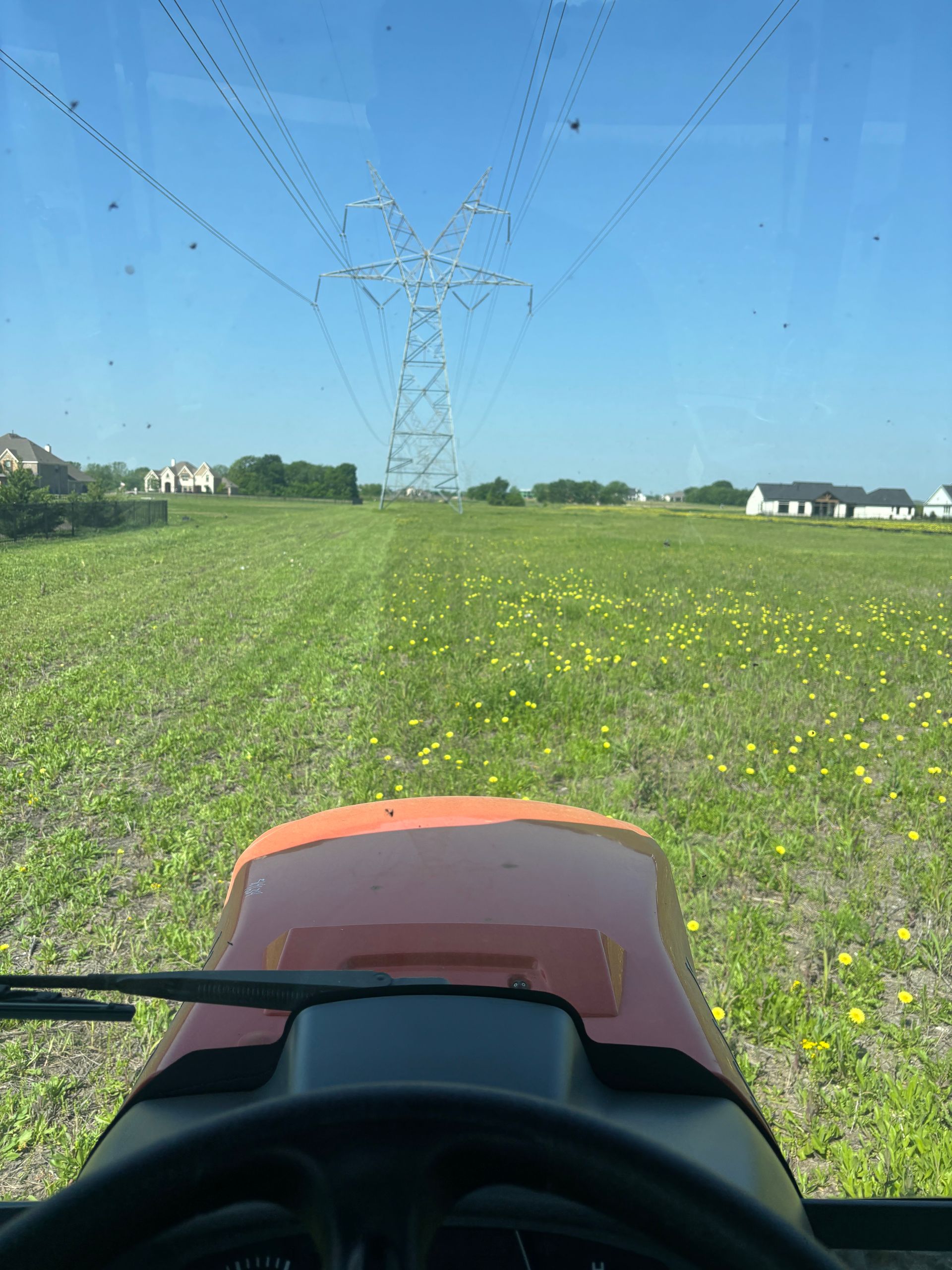 View from a tractor driving through a green field under power lines on a clear blue day
