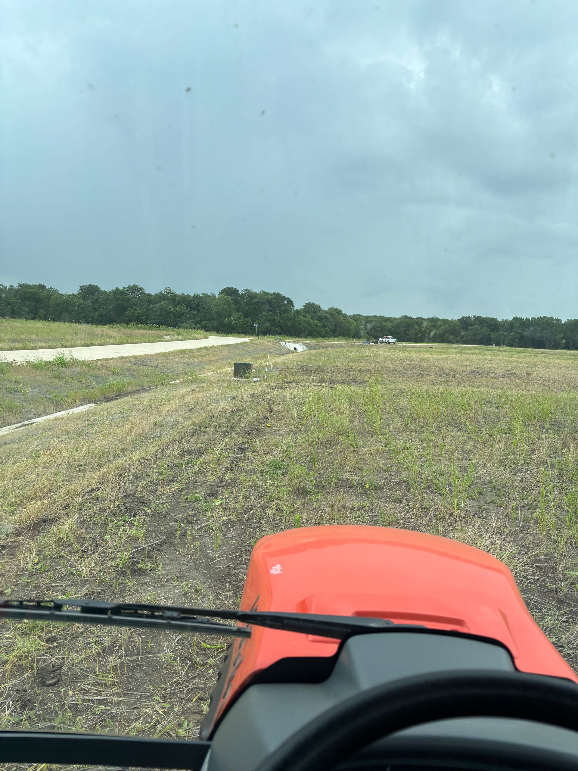 View from a red tractor driving along a muddy field under a cloudy sky