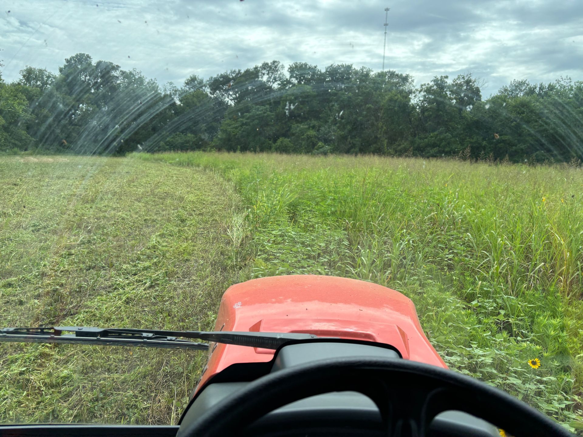 View from a red tractor driving through a grassy field with water spraying from the left side