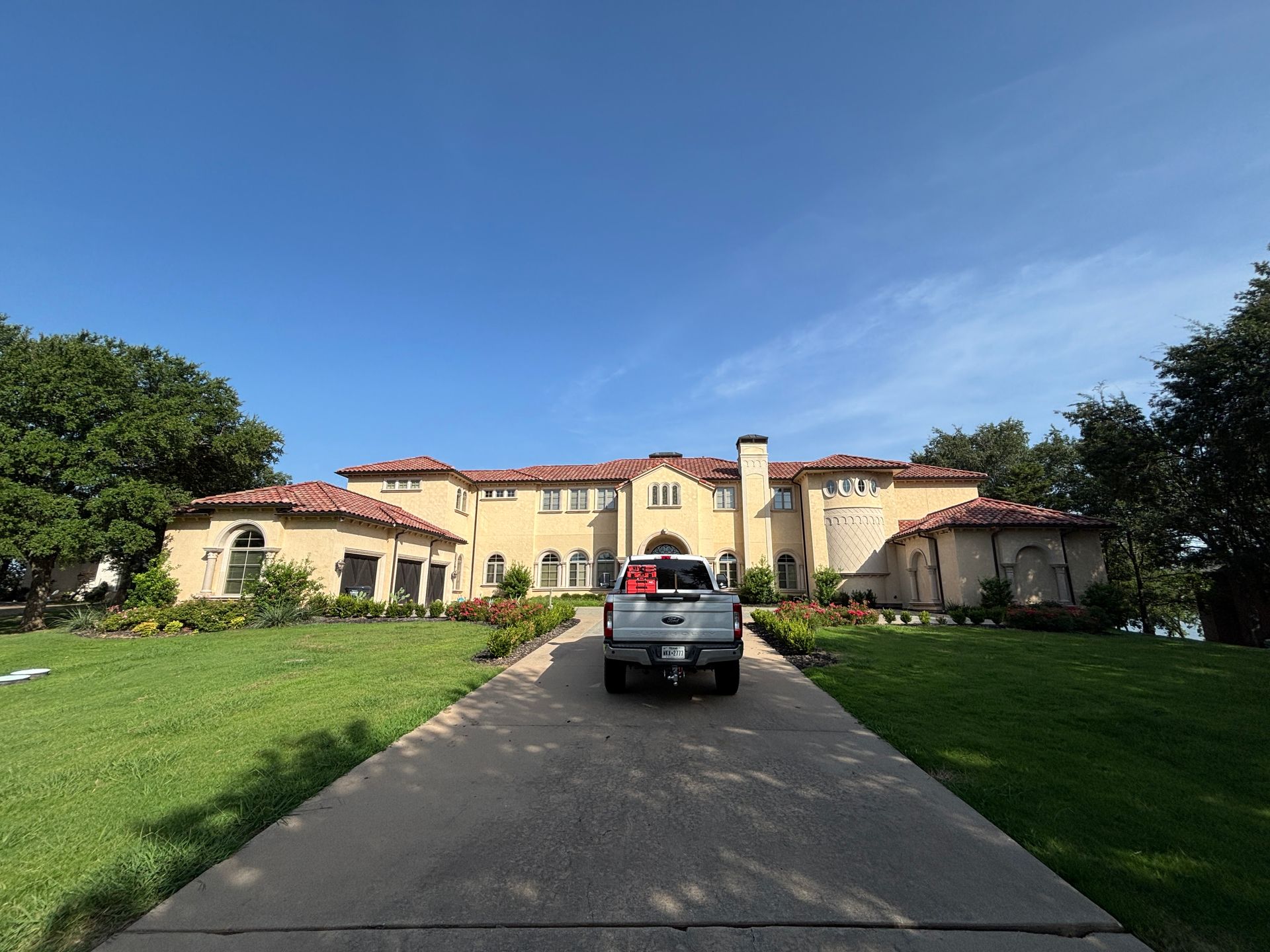 Black SUV on driveway leading to a large yellow villa with red-tile roofs under a clear blue sky