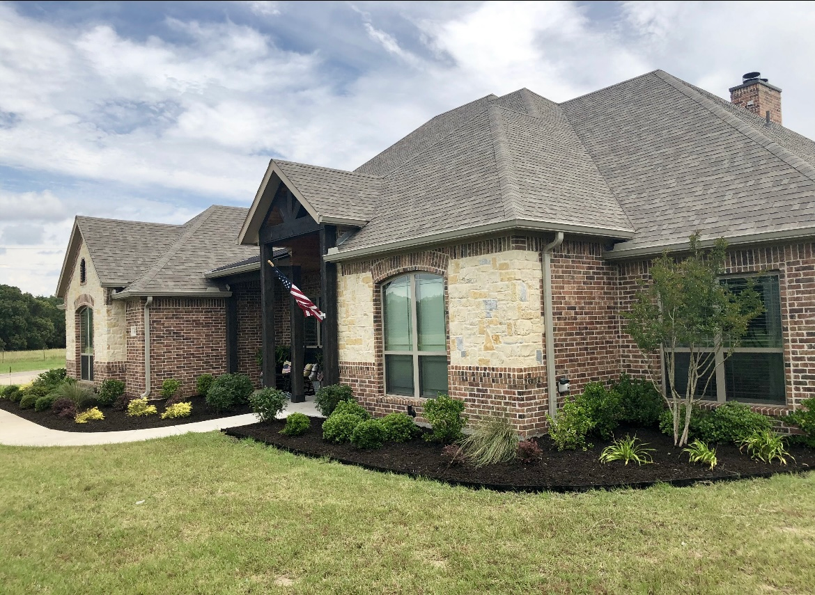 Brick and stone house with a curved roof and landscaped front yard