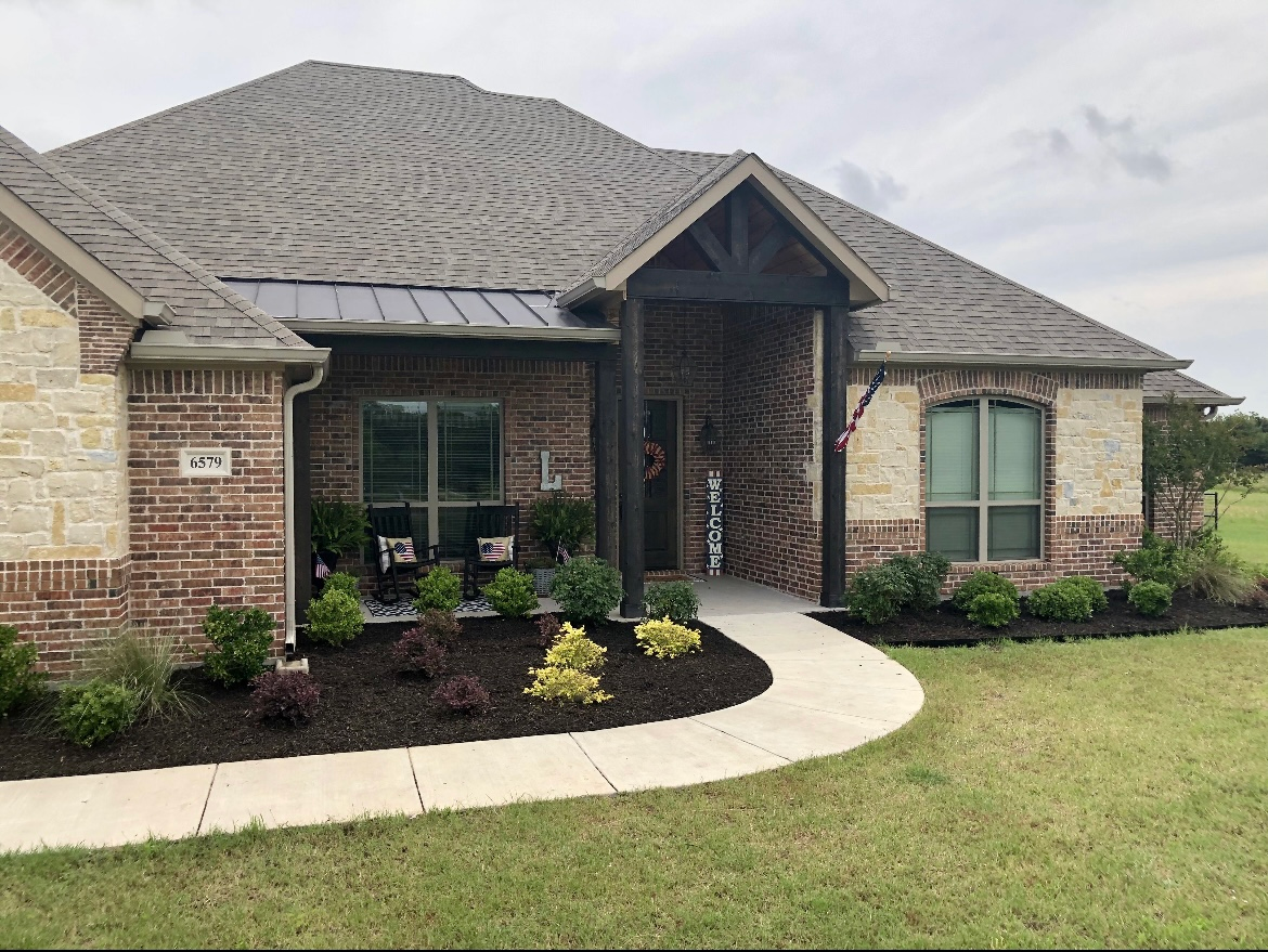 Suburban brick-and-stone house with a curved walkway, front porch, and manicured lawn