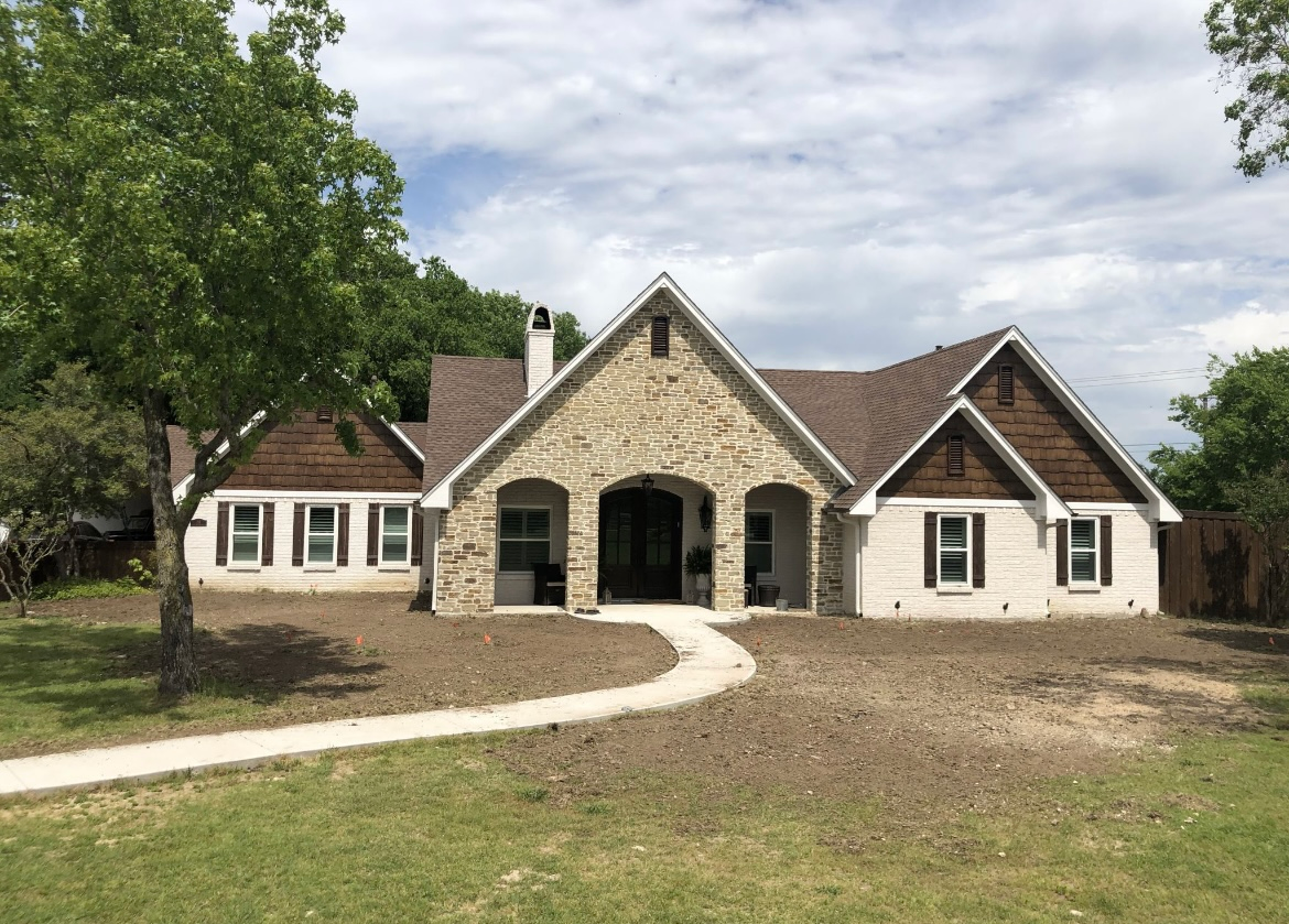 Stone house with arched front porch, white siding wings, and a curved walkway amid a grassy yard